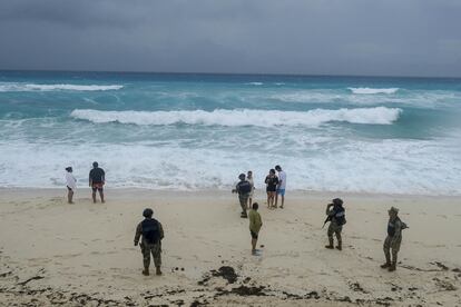 Turistas y miembros del Ejército Mexicano observan el cielo nublado y en el horizonte del mar desde las playas de Cancún, ante la proximidad de 'Helene', aún como tormenta tropical, este martes. 