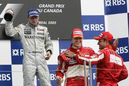 Kimi Raikkonen levanta, serio, su botella de champaña mientras Michael Schumacher y Ruben Barrichello se felicitan sonrientes.