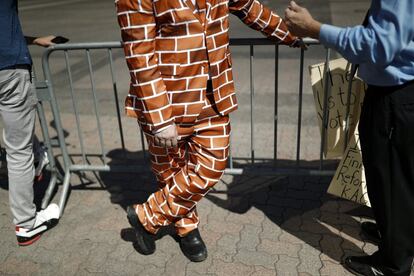 Una persona viste un traje con el patrón de una pared de ladrillos mientras espera con otros partidarios la llegada del presidente Donald Trump.