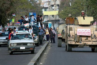 Una caravana electoral de partidarios del gran ayatolá Ali al Sistani pasa junto a un convoy militar de EE UU en Bagdad.