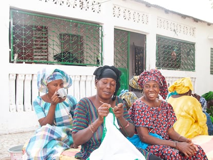 Mujeres sentadas esperan que comience la reunión, tomando café, hablando y haciendo ganchillo en el patio de Fatou Thiam.
