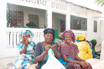 Mujeres sentadas esperan que comience la reunión, tomando café, hablando y haciendo ganchillo en el patio de Fatou Thiam.