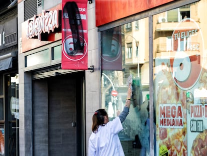 Una trabajadora borra varias pintadas en los cristales del local de Telepizza situado en la calle Bravo Murillo, en Madrid.