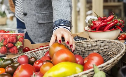 Una mujer coge un tomate de una cesta de verduras. 