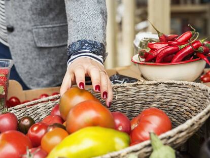 Una mujer coge un tomate de una cesta de verduras. 