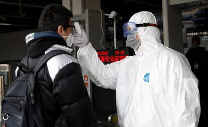 Un trabajador con traje de protección utiliza un termómetro para medir la temperatura de un viajero en la estación de metro de Xizhimen en Pekín.