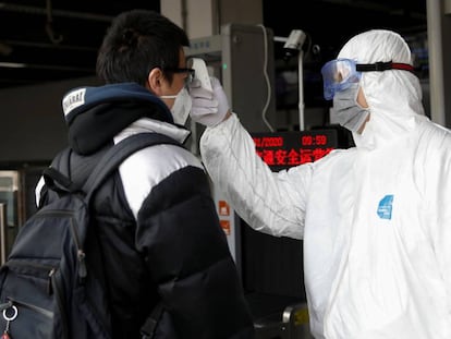 Un trabajador con traje de protección utiliza un termómetro para medir la temperatura de un viajero en la estación de metro de Xizhimen en Pekín.