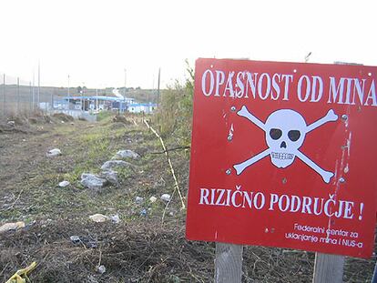 Un cartel oficial avisa del peligro de minas en un descampado cerca de Bihac, en el noroeste de Bosnia-Herzegovina. Se conocen 18.600 lugares como éste. Al fondo, el puesto de la frontera con Croacia.
