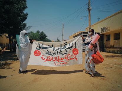 Dos mujeres se preparan para participar en la primera protesta después de cuatro meses de confinamiento por la covid-19. Miles de sudanesas salieron a las calles a demandar que se respeten las reivindicaciones de la revolución. El cartel las identifica como miembros de la Unión Sudanesa de Mujeres, la organización que logró el derecho a voto para las mujeres en 1964.