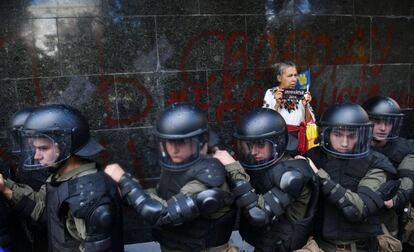 Una mujer se para junto a la policía antidisturbios ucraniana frente a la Oficina del Fiscal General en Kiev para evitar ataques de activistas de los grupos de extrema.