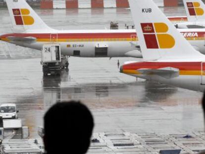 Dos pasajeros observan varios aviones de la compañia Iberia en el aeropuerto de Barajas.