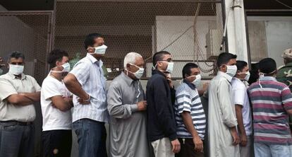 Hombres libios con mascarilla médica esperan para ver el cuerpo muerto de Muammar Gaddafi.
