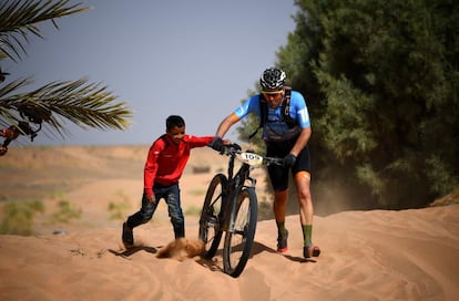 Un niño ayuda a un competidor a empujar su bicicleta durante la primera etapa de la carrera, el 28 de abril de 2019, en Merzouga.