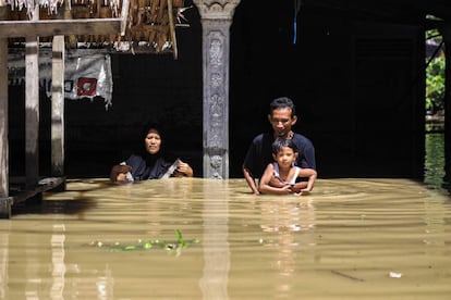 A family walks through a flooded residential area in Gampong Meunasah, Indonesia.