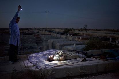 Serie 'En medio del infierno. La población civil siria en guerra'. Un soldado de las Fuerzas Sirias alumbra con una linterna el cadáver de un hombre desconocido, asesinado por la artillería del ejército sirio, en el cementerio de Aleppo, antes de enterrarlo en una fosa común, Siria (13 de octubre de 2012).
