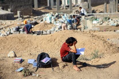 Un alumno yemení estudia al aire libre mientras otros estudiantes asisten a clases en edificios residenciales y comerciales convertidos en una escuela y aulas aún sin terminar en Tae, Yemen.