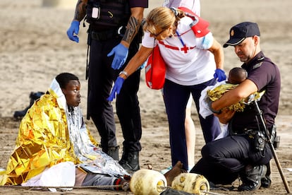 Dos policías y una trabajadora de la Cruz Roja atienden a los migrantes llegados en cayuco. 