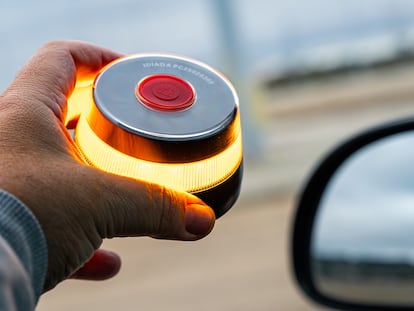 La mano de un hombre sacando la baliza por la ventanilla de su coche.