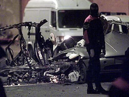 Un agente de la Ertzaintza, ante los restos del coche destrozado tras la explosión en Bilbao. PLANO GENERAL