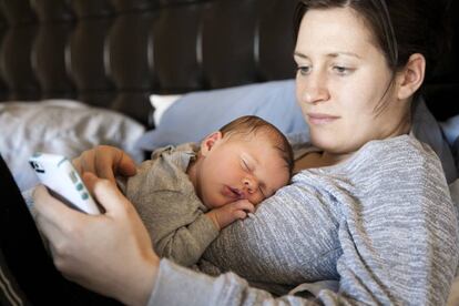 Una madre mira el m&oacute;vil mientras su beb&eacute; duerme. 