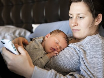 Una madre mira el m&oacute;vil mientras su beb&eacute; duerme. 