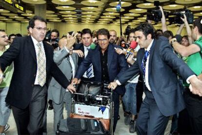 Fabio Capello, en el centro, trata de sortear el acoso de los periodistas a su llegada al aeropuerto de Barajas.