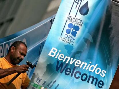 Un trabajador venezolano sostiene un cartel de bienvenida delante del Ministerio venezolano de Energía en Caracas, con motivo de la cumbre ministerial de la OPEP de este jueves.