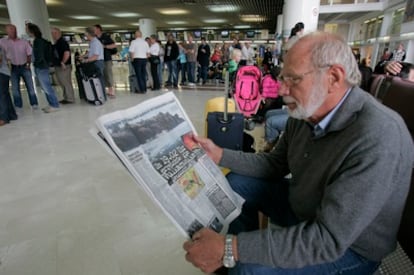 Un pasajero lee un periódico mientras espera en el aeropuerto de Alicante, donde se han formado largas colas por la anulación de vuelos.