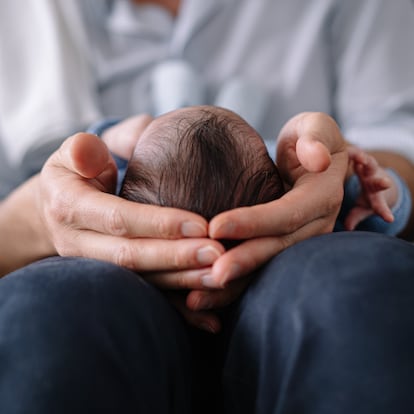 Horizontal detail of unrecognizable caucasian father holding baby head with tenderness at home. Family lifestyles