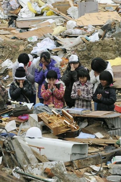 Unos niños supervivientes guardan un minuto de silencio en medio de los escombros a las 14.26 horas, exactamente un mes después de que la tierra temblara, en el area de Miyako, Iwate.