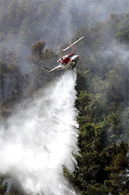 Un helicóptero remoja, ayer por la mañana, la zona del incendio para evitar que se reaviven las llamas.