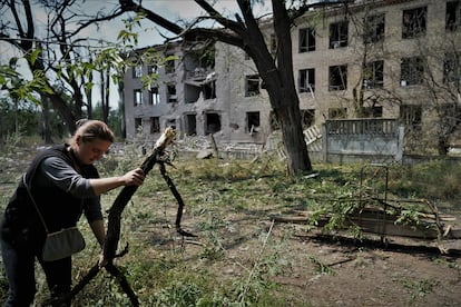 Olga, de 45 años, recoge leña y maderas tras el bombardeo de un colegio (detrás) por la aviación rusa esa misma mañana en Toretsk.