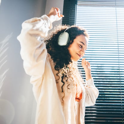 A curly girl in headphones dances near the window.