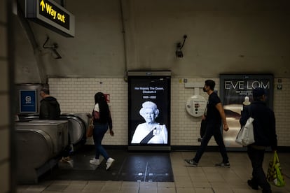 Varias personas pasan delante de una marquesina con el retrato de Isabel II en el metro de Londres.
