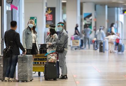 Varias personas protegidas con mascarillas y pantallas protectoras en el aeropuerto Madrid-Barajas.