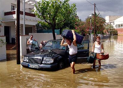 Una familia extranjera intenta extraer sus pertenencias del vehículo en una calle de Coma-ruga inundada por la lluvia.