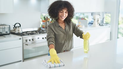 Mujer limpiando la cocina con un paño y un desinfectante.
