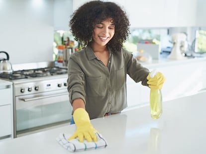 Mujer limpiando la cocina con un paño y un desinfectante.