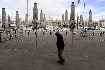 Un hombre camina frente a la terraza cerrada de un restaurante del puerto de Marsella. 