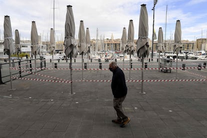 Un hombre camina frente a la terraza cerrada de un restaurante del puerto de Marsella. 