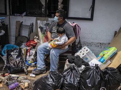 Un hombre cuida de un bebé al exterior de su casa que quedó dañada por las fuertes lluvias de la tarde el lunes en Atizapán, Estado de México