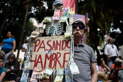 Un partidario de la oposición venezolana sostiene una pancarta con la imagen del esqueleto humano, los carteles de Bolívar se adjuntan a ella y una leyenda que dice "pasando hambre" mientras espera en la plaza Bolívar en Chacao, al este de Caracas, para escuchar a Guaidó.