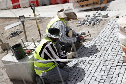Dos obreros de la construcción pavimentan la acera en la calle Alcalá, este lunes en Madrid. 