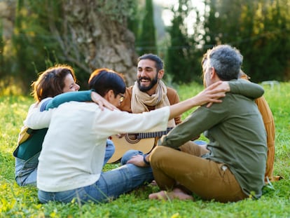 Un grupo de amigos cantando y tocando música con la guitarra sentados en el campo.