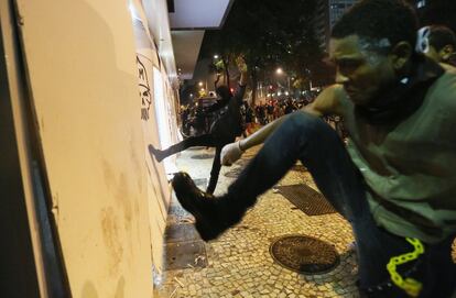 Unos manifestantes patean unos tablones que protegen una sucursal bancaria en Río de Janeiro (Brasil) durante la protesta, 8 de octubre de 2013. Pese a que los profesores, que llevan 60 días en huelga, y miles de estudiantes marcharon pacíficamente por la avenida Rio Branco desde la iglesia de la Candelaria hasta la Cinelandia, pequeños grupos de encapuchados se infiltraron entre los manifestantes y provocaron a la policía.