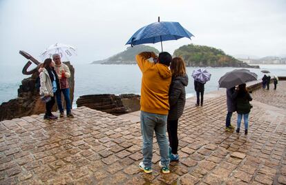 Varios turistas con paraguas visitan el Peine del Viento, en San Sebastián, este domingo.