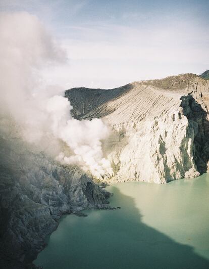 Situado al este de la isla indonesia de Java y con 2.386 metros de altitud, el volcán Kawah Ijen es un lugar contradictorio: onírico y letal a la vez. Desde las alturas se puede observar la extraña y fascinante combinación del amarillo del azufre, el turquesa de las aguas y unas preciosas llamas azules que solo aparecen por la noche para regocijo de turistas llegados de todo el mundo. Pero este paisaje sobrenatural esconde una cara oculta: las aguas del hermoso lago están cargadas de ácido sulfúrico y de ácido clorhídrico y son altamente tóxicas. En cuanto al embrujo de su fuego azul, puede decirse que es tan mágico como peligroso, ya que desprende dióxido de azufre: un gas altamente venenoso e irritante y uno de los principales causantes de la lluvia ácida. Pero el contraste de Kawah Ijen no acaba solo en el paisaje. Los visitantes que se acercan cada noche para contemplar las llamas azules conviven con centenares de mineros locales que se exponen diariamente a estos gases y vapores tóxicos para cargar con grandes bloques de azufre bajo un aire irrespirable. Por apenas cuatro euros diarios, transportan cestas de bambú llenas de azufre que venden al peso a una empresa minera que multiplica el precio de ese material por 10. El azufre es destinado a blanquear azúcar y a la fabricación de cerillas, fuegos artificiales, cosméticos y dinamita.