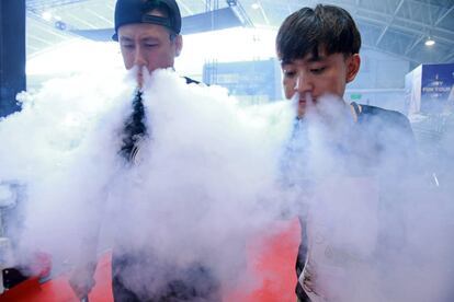 Vendedores exhalando vapores al tiempo que muestran sus productos de cigarrillos electrónicos en el China International Exhibition Center en Pekín.