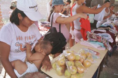 Una mujer amamanta a su bebé y canjea verduras en un centro de trueque de Buenos Aires.