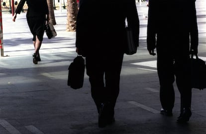 Un mujer y dos hombres de negocios pasean por una calle.